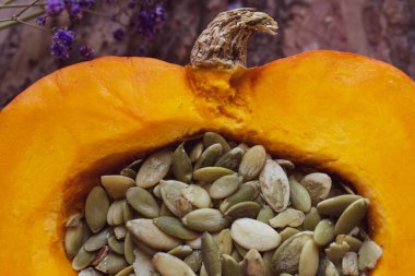 Çekirdekli parlak portakal suyu kaplı bir balkabağı. Koyu zıt zıt arka planda kesilmiş ağaç kabuğu ve küçük mor çingene çiçekleri.