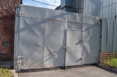 Old gray metal old gate and a closed door on an iron fence in the grass on a city street