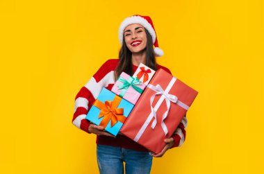 Güzel, heyecanlı, gülümseyen bir kadının fotoğrafını çek. Elinde bir sürü güzel Noel hediyesi kutusuyla. Eğlenirken ve sarı arka planda poz verirken. 