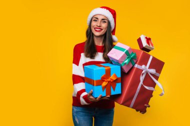Güzel, heyecanlı, gülümseyen bir kadının fotoğrafını çek. Elinde bir sürü güzel Noel hediyesi kutusuyla. Eğlenirken ve sarı arka planda poz verirken. 