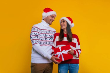 Yeni yılı kutlarken ve birbirlerine hediyeler verirken ellerinde hediye kutularıyla Noel kıyafetleri içinde güzel mutlu ve heyecanlı genç bir çiftin fotoğrafını çek.