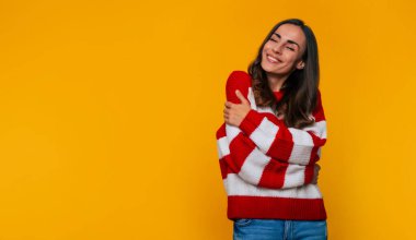 Sarı arka planda poz verirken, eğlenirken ve yalnızken çizgili süveter giyen mutlu ve güzel bir kadının fotoğrafını çek.
