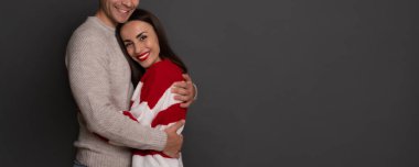 Birbirlerine sarılıp gri arka planda poz verirken birbirlerine aşık güzel bir çiftin portresi. Romantik, aşk, ilişki ve Sevgililer Günü konsepti..