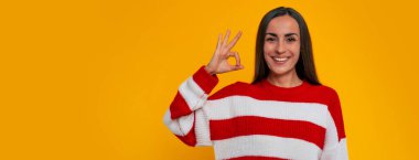 Resmin afişi mutlu, güzel esmer kadın kamerada gülümseyerek büyük bir işaret gösteriyor.