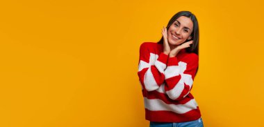 O kadar mutluyum ki! Gülümseyen güzel bir kadının portresi avuçlarını yanaklarında tutarken ve sarı arka planda kameraya bakarken