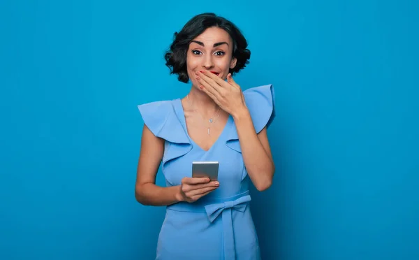 オンラインだ アプリだ タイピング 通信だ インターネット ユーザー 閉じる上のポートレートの笑顔かわいいですスタイリッシュなブルネット女性とともに現代的なスマートフォンで手に隔離された青の背景 — ストック写真