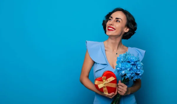 女性の日だ バレンタインデーよ エレガントなファッショナブルな笑顔の女性の肖像画を閉じますドレスに花の束とギフトボックスで手に隔離された青の背景 ストック写真