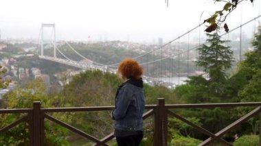 İstanbul 'a bakan Türk kadın, Fatih Sultan Mehmet Köprüsü ile gökyüzüne bakıyor. Ayrıca İkinci Boğaz Köprüsü olarak da bilinir, İstanbul, Türkiye Boğazı boyunca uzanır..