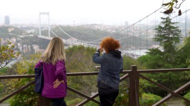 2 Turkish women looking at Istanbul skyline with Fatih Sultan Mehmet Bridge. Also known as the Second Bosphorus Bridge, it spans the Bosphorus strait, Istanbul, Turkey.