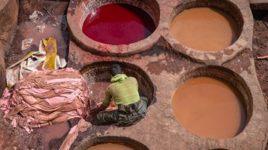 Fez, Fas - Nisan 2018: Tanner Chouara Tannery 'de boya kaplarında hayvan derileri boyuyor. Yuvarlak taş kuyuları boyayla ya da derileri yumuşatmak için beyaz sıvılarla dolu..