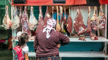 Osh, Kyrgyzstan - May 2022: Unidentified woman examines a variety of open air meat in a butcher shop at local market