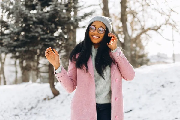 Молодая Афроамериканка Очках Теплых Варежках Говорит Телефону Показывает Копировальном Пространстве — стоковое фото