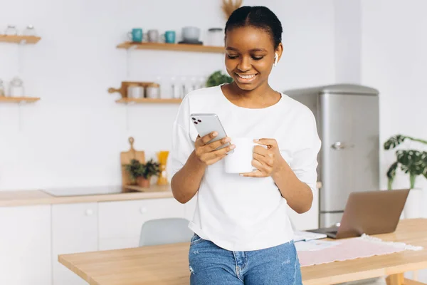 Neşeli Genç Siyah Bir Kadının Portresi Elinde Telefon Mutfakta Kahve — Stok fotoğraf