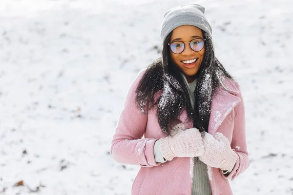 身穿眼镜和手套的非洲裔美籍年轻女子是一个快乐而积极的女孩的画像 她穿着温暖的衣服 在寒冷 寒冷的冬雪公园里微笑着 冬季概念 — 图库照片