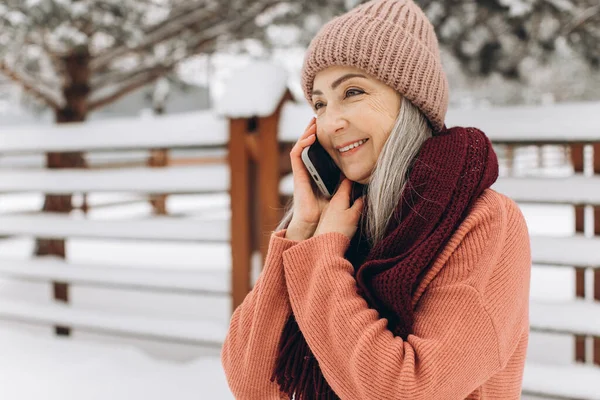 穿着针织毛衣 围巾和帽子 头发灰白的老妇人在冬天的背景下通过电话交谈 — 图库照片