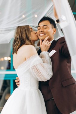 Düğün günü. Güzel Avrupalı gelin ve Asyalı damadı kafelerin ve büyük pencerelerin önünde poz veriyorlar..