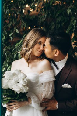 Düğün günü. Güzel Avrupalı gelin ve Asyalı damadı kafelerin ve büyük pencerelerin önünde poz veriyorlar..