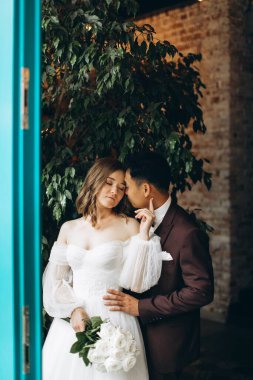 Düğün günü. Güzel Avrupalı gelin ve Asyalı damadı kafelerin ve büyük pencerelerin önünde poz veriyorlar..