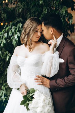 Düğün günü. Güzel Avrupalı gelin ve Asyalı damadı kafelerin ve büyük pencerelerin önünde poz veriyorlar..