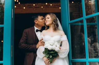 Düğün günü. Güzel Avrupalı gelin ve Asyalı damadı kafelerin ve büyük pencerelerin önünde poz veriyorlar..