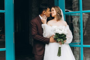 Düğün günü. Güzel Avrupalı gelin ve Asyalı damadı kafelerin ve büyük pencerelerin önünde poz veriyorlar..