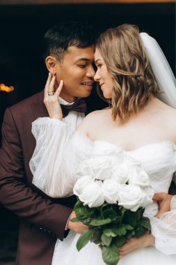 Düğün günü. Güzel Avrupalı gelin ve Asyalı damadı kafelerin ve büyük pencerelerin önünde poz veriyorlar..