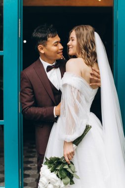 Düğün günü. Güzel Avrupalı gelin ve Asyalı damadı kafelerin ve büyük pencerelerin önünde poz veriyorlar..
