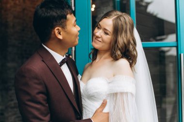 Düğün günü. Güzel Avrupalı gelin ve Asyalı damadı kafelerin ve büyük pencerelerin önünde poz veriyorlar..