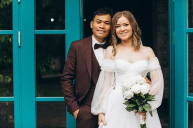 Düğün günü. Güzel Avrupalı gelin ve Asyalı damadı kafelerin ve büyük pencerelerin önünde poz veriyorlar..