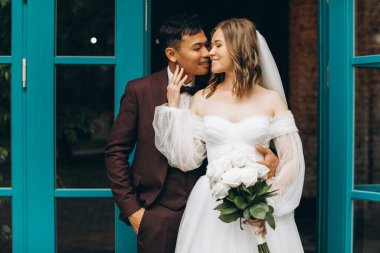 Düğün günü. Güzel Avrupalı gelin ve Asyalı damadı kafelerin ve büyük pencerelerin önünde poz veriyorlar..