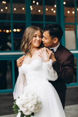 Düğün günü. Güzel Avrupalı gelin ve Asyalı damadı kafelerin ve büyük pencerelerin önünde poz veriyorlar..