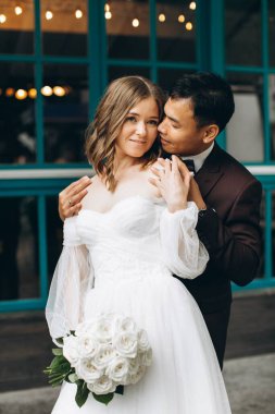 Düğün günü. Güzel Avrupalı gelin ve Asyalı damadı kafelerin ve büyük pencerelerin önünde poz veriyorlar..