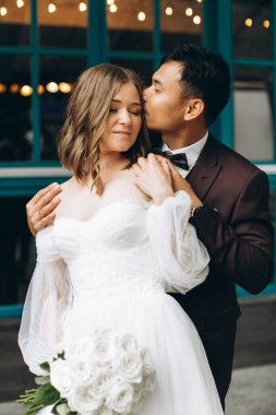 Düğün günü. Güzel Avrupalı gelin ve Asyalı damadı kafelerin ve büyük pencerelerin önünde poz veriyorlar..