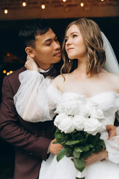 結婚式の日 美しいヨーロッパの花嫁と彼女のアジアの新郎は カフェや大きな窓を背景にポーズ — ストック写真