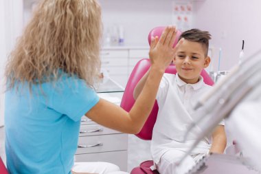 Çocuk gülüyor ve dişçilik muayenesinden sonra bir kadın dişçiye saygı gösteriyor.