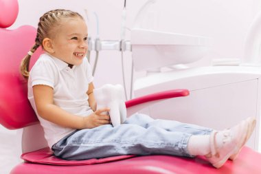 Dişçiye giderken gülümseyen küçük kız diş kliniğinde diş modelini tutuyor.