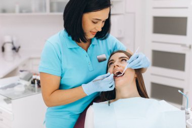 Kadın dişçi, dişçi koltuğunda hastasını muayene ediyor..