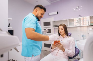 Dişçi gülümser ve kıza dişleri olan bir model gösterir, implantasyondan ve bakterilerden bahseder..