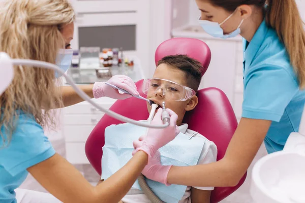 女性歯科医は歯科クリニックで男の子の歯を治療します — ストック写真
