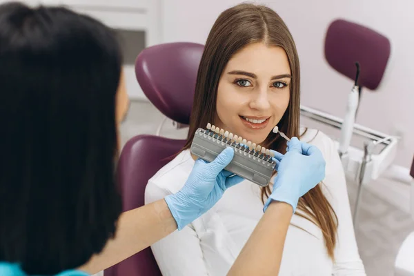 A female dentist helps her patient choose the color of the implant or crown using a color scale