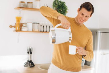 Sarı günlük elbiseli yakışıklı bir adam evde oturmuş kahve içiyor.