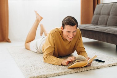 Sarı elbiseli yakışıklı genç adam evde oturmuş kitap okuyor.