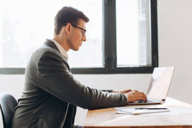 Gözlüklü modern ciddi adam, dizüstü bilgisayarla çalışan ofis çalışanı.