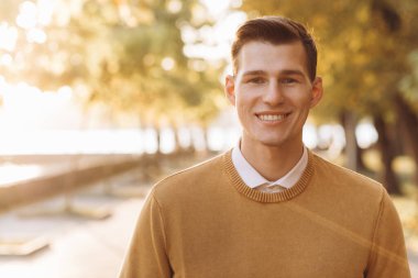 Günbatımında parkta poz veren sarı ve beyaz elbiseli modern yakışıklı adam.