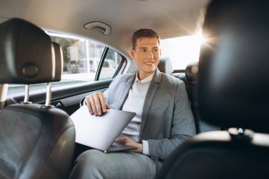 Modern bir iş adamı bir arabanın arka koltuğunda otururken dizüstü bilgisayar kullanıyor..
