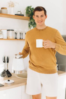 Sarı günlük elbiseli yakışıklı bir adam evde oturmuş kahve içiyor.