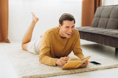 Sarı elbiseli yakışıklı genç adam evde oturmuş kitap okuyor.