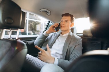 Genç işadamı arabanın arka koltuğunda otururken cep telefonuyla konuşuyor..