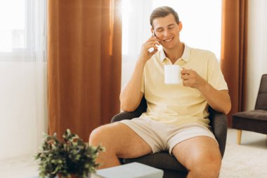 Sarı giysili yakışıklı bir adam evde oturmuş telefonda konuşuyor.