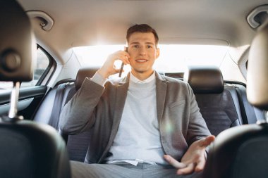 Genç işadamı arabanın arka koltuğunda otururken cep telefonuyla konuşuyor..